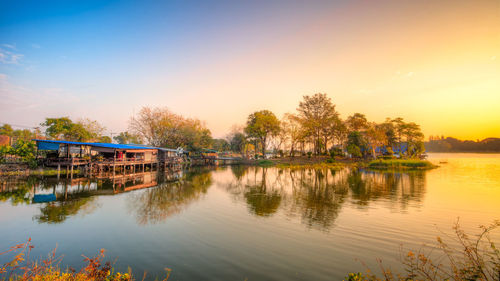 Scenic view of river by houses against sky during sunset