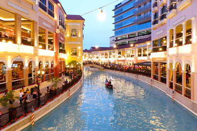 People on illuminated canal amidst buildings in city