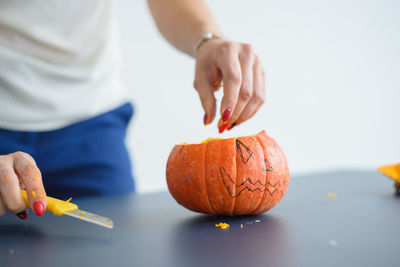 Midsection of man holding pumpkin against wall during halloween