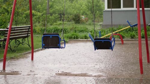 Empty swing drenches in the rain, swaying in wind. a heavy rain, a downpour with a strong wind.