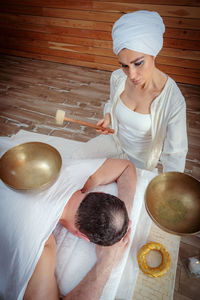 A woman performs tibetan singing bowl therapy with a man lying under a white sheet. 