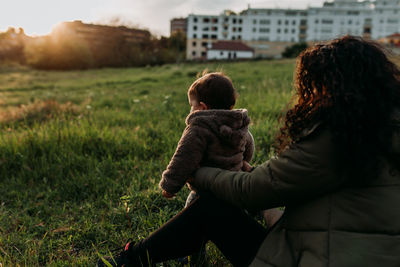 Rear view of mother and daughter on grass against sky