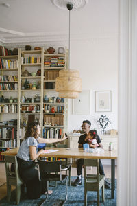 Woman showing mobile phone to young man sitting with daughter at table in house