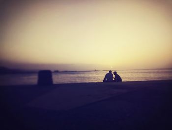 Silhouette couple on sea shore against sky during sunset