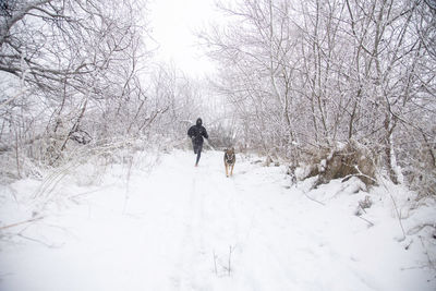 Rear view of person walking on snow covered field