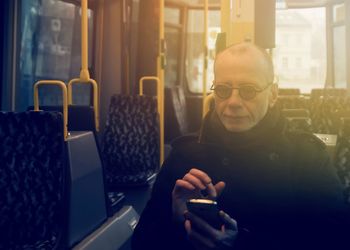 Mature man using mobile phone while sitting in bus