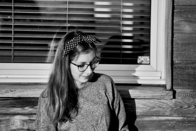 Teenage girl looking down while standing against window