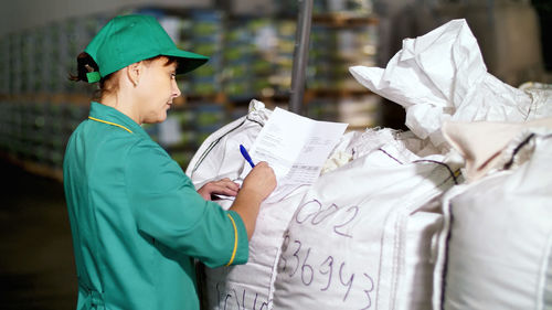 Portrait of woman, employee of agricultural enterprise, fills out paper sheets on big bags in the