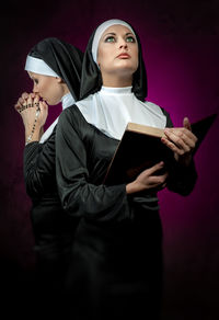 Young nuns with bible and rosary beads standing against colored background
