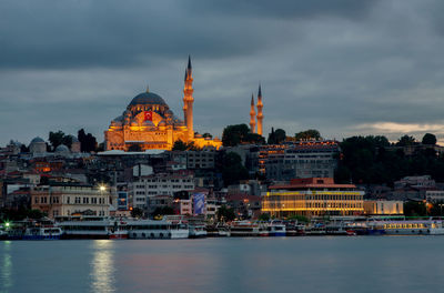 Strait by buildings and mosques against cloudy sky