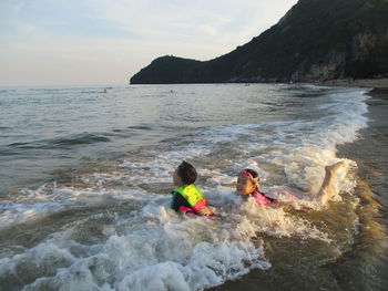 People on rock in sea against sky