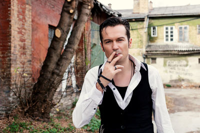 Self-confident retro-styled man smoking cigarette outdoors and looking at camera.