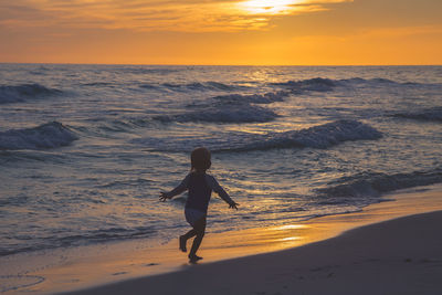 Child running on beach against sky during sunset