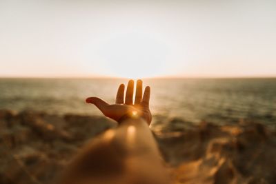 Cropped hand against sea during sunset