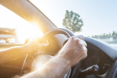 Cropped hands of man holding steering wheel in car