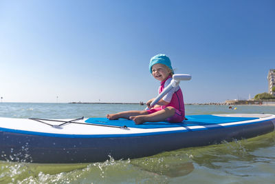 Full length of happy girl paddleboarding on sea against clear blue sky