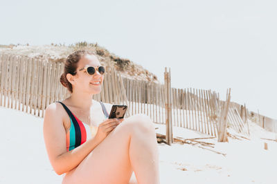 Young woman wearing sunglasses while standing against clear sky