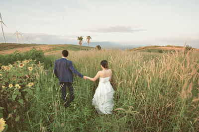 Young couple walking on grassy field against sky