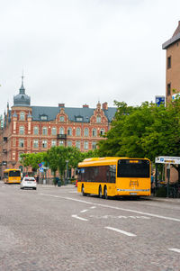 Cars on road by buildings in city against sky