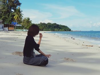 Woman sitting at beach against sky