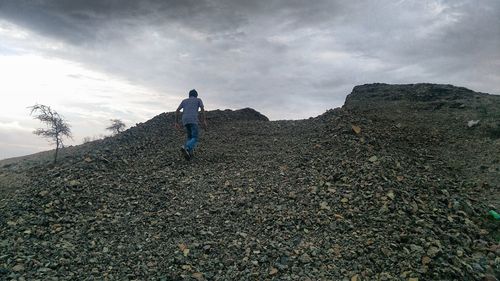 Low angle view of man walking on hill against cloudy sky during sunset