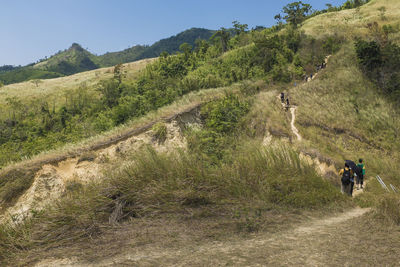 Rear view of people walking on field by mountain