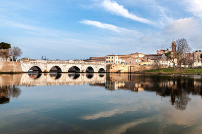 Arch bridge over river by buildings against sky