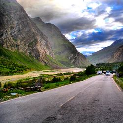 Road leading towards mountain against cloudy sky