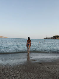 Rear view of woman standing at beach against clear sky