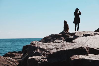 People standing on cliff by sea against clear sky