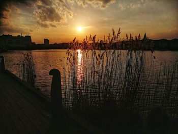 Silhouette wooden posts in lake against sky during sunset