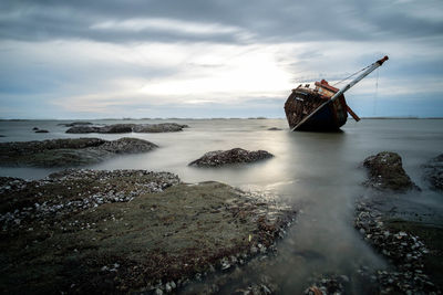 Abandoned boat in sea against sky