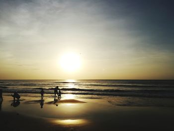 Silhouette people standing on beach against sky during sunset