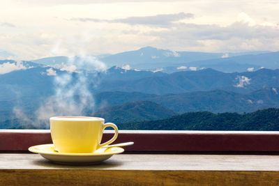 Close-up of coffee cup on window sill against mountains