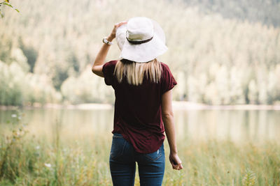 Rear view of woman standing by plants and lake