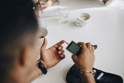 Businessman checking blood sugar level with glaucometer at table