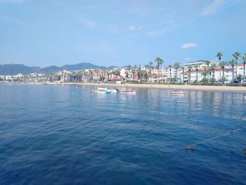 Sailboats in sea by townscape against sky