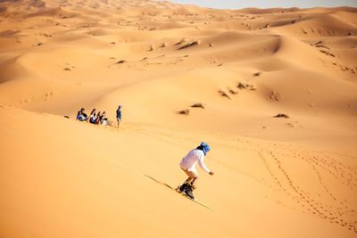 Person sandboarding in desert against clear sky