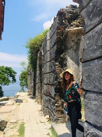 Full length portrait of woman standing against sky, backing up with ruins