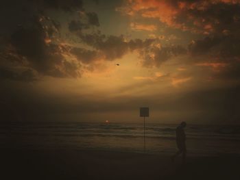 Silhouette man standing on beach against sky during sunset