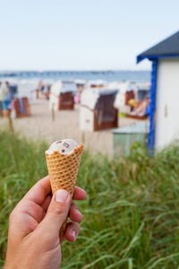 Cropped hand holding ice cream against hooded chairs at beach