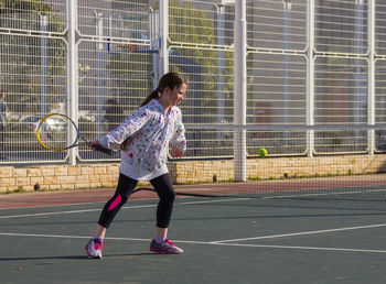 Full length of girl playing tennis in court