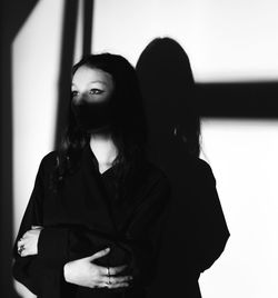 Young woman looking away while standing against wall