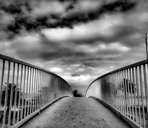 Road leading towards building against cloudy sky
