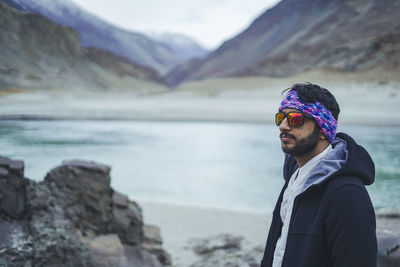 Young handsome indian male with trekking gears posing in front of a camera with mountains.