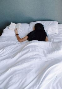 Woman holding book while sleeping on bed at home