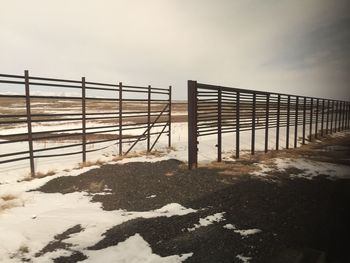 Fence on snow covered field against sky