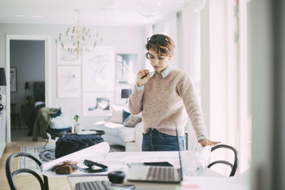 Woman standing at table with blueprint working at home