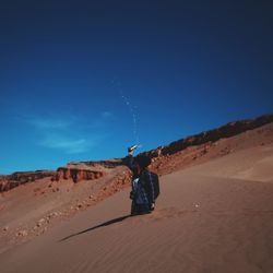 Woman throwing water while standing in sand against blue sky