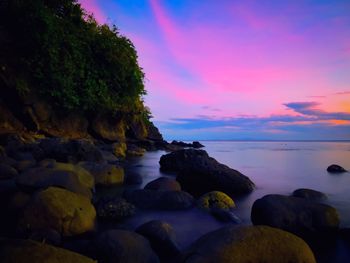 Rocks at sea shore against sky during sunset